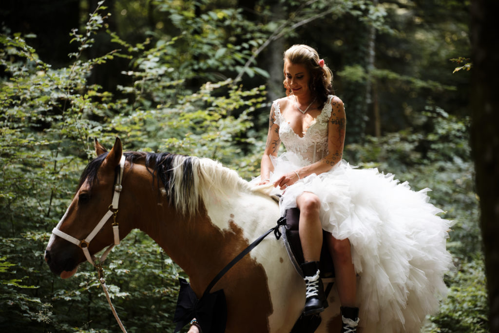 Mariée tatouée à cheval sur son mustang, dans la forêt